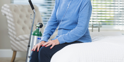 Photo of unknown person sitting on endge of bed with an oxygen tank