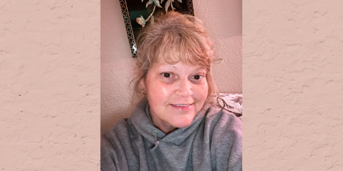 Close up selfie of a white woman with blond hair smiling wearing a gray hoodie.