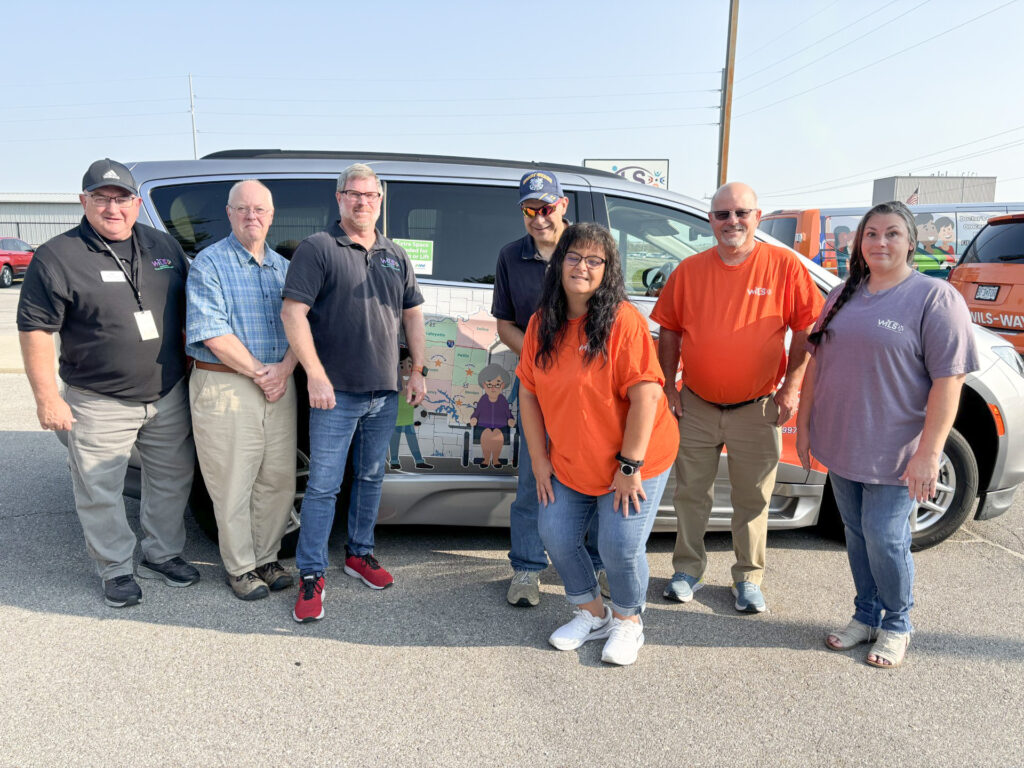 WILS transportation team stands outside in front of a WILS van.