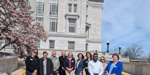 WILS staff, volunteers, and consumers outside of the Missouri state capitol building beside a blooming pink magnolia tree.