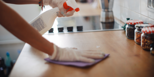 Photo of someone wearing cleaning gloves spraying a kitchen counter with cleaner and wiping it down.