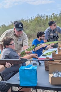 Volunteers stand beside a table full of participants assisting with target practice.