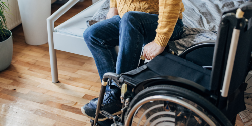 Photo of man in jeans and a yellow shirt transferring from his bed to his wheelchair