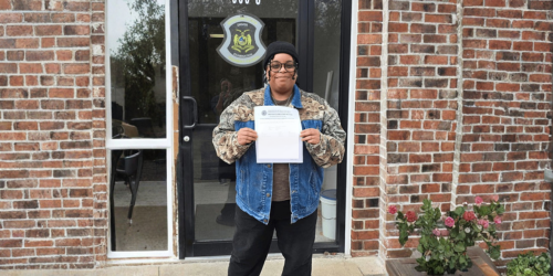 Womens stands outside brick building holding a piece of paper.