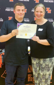 Photo of male high school senior with brown hair wearing a black polo poses with a female WILS staff member with blond hair and a black shirt while smiling and holding a scholarship certificate.